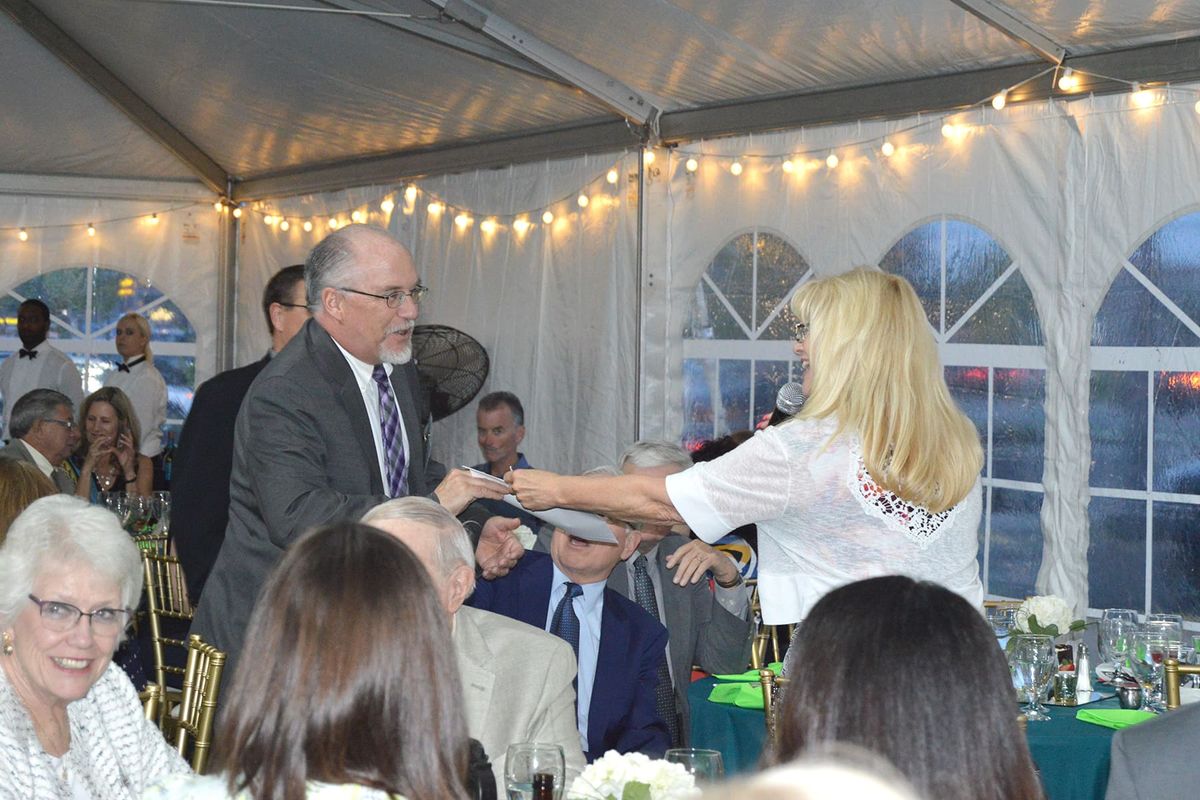 A formal gathering where two people are dancing under a tent with string lights.