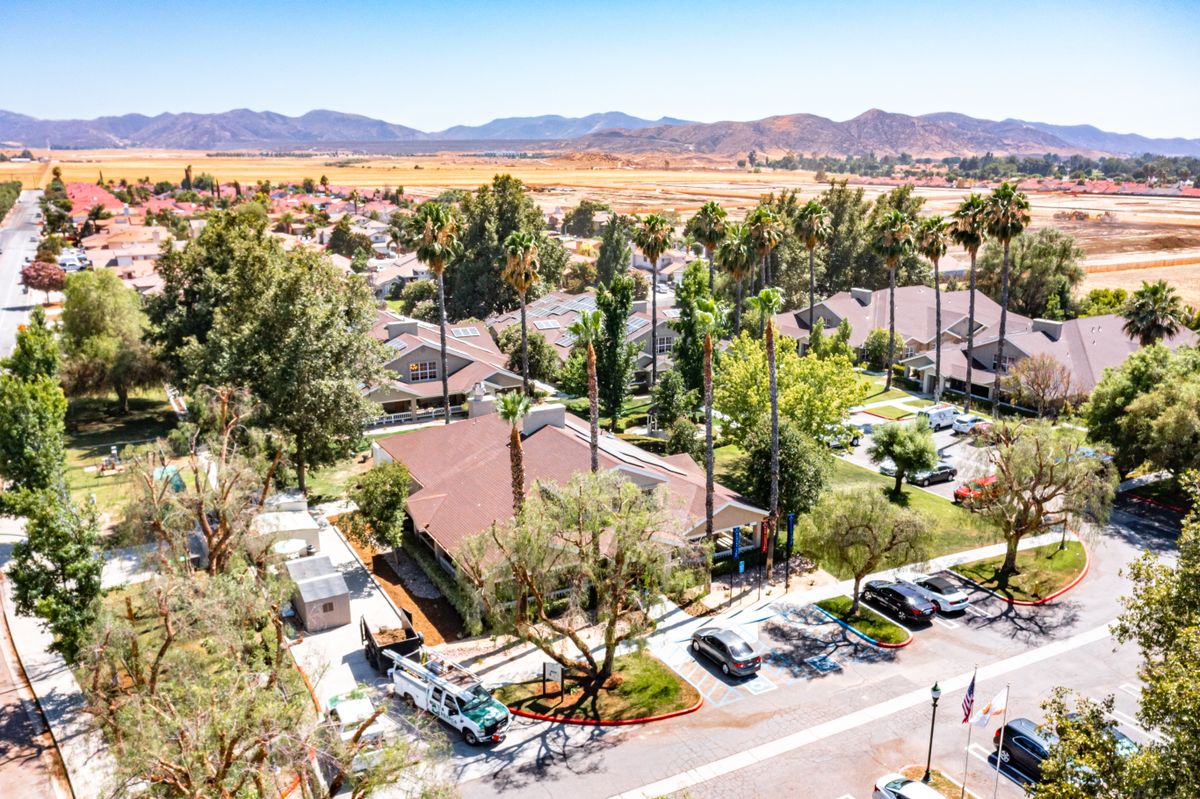 Aerial view of a residential neighborhood with houses, trees, and parked vehicles, surrounded by scenic mountains in the background.