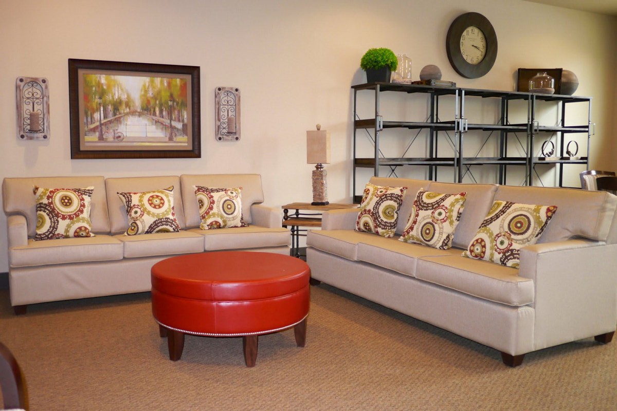 A modern living room setup with neutral-toned sofas, colorful cushions, a red round coffee table, and wall art.