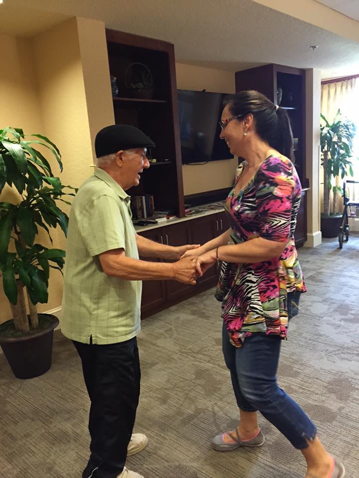 An elderly man and a woman enjoy dancing together indoors.