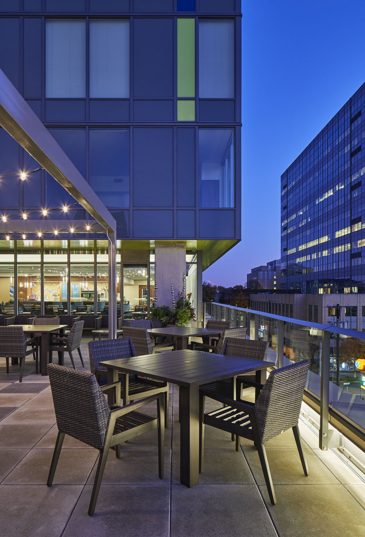 A modern rooftop terrace with tables and chairs, overlooking a cityscape at dusk.