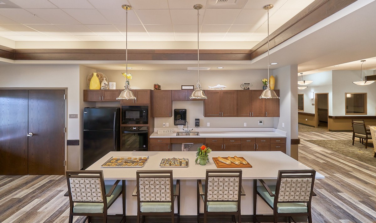 A modern kitchen with sleek cabinetry, pendant lighting, and a spacious countertop with bar stools.