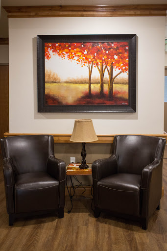 A cozy seating area featuring two leather chairs, a side table with a lamp, and a vibrant painting of trees in autumn colors.