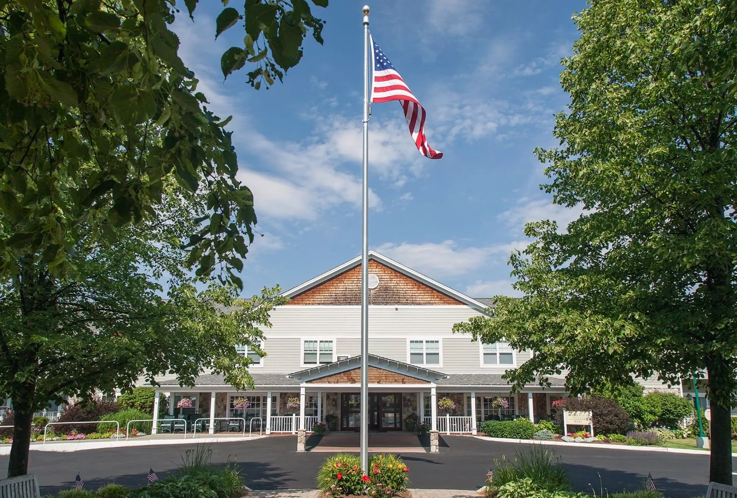 A building with an American flag flying in front, surrounded by trees under a blue sky.