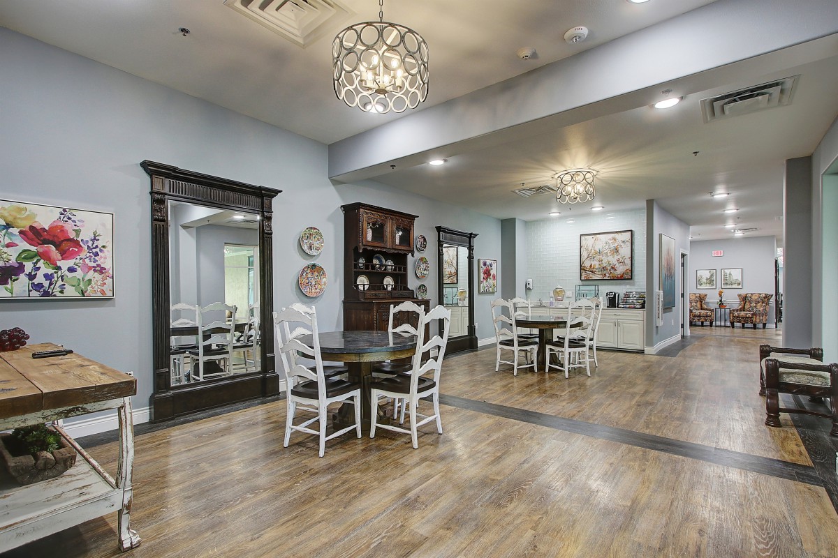 A spacious and well-lit dining area with wooden flooring, furnished with tables and chairs, adorned with elegant chandeliers.