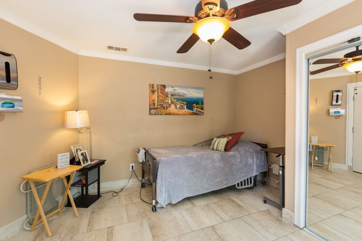 A cozy bedroom featuring a single bed and ceiling fan, with warm beige walls and decorative artwork.