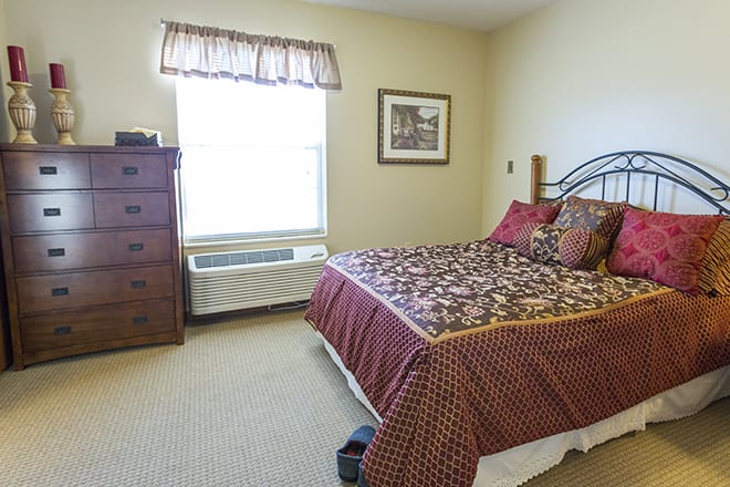 A cozy bedroom with a decorative bedspread and a dresser by the window.