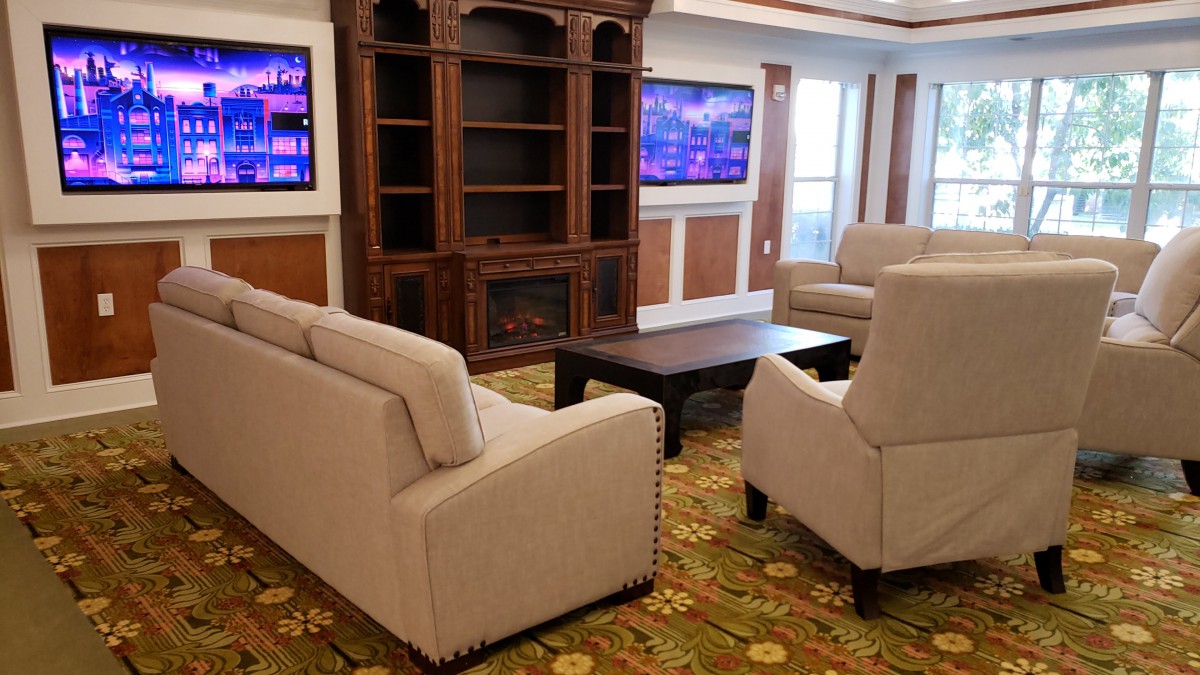 A cozy living room featuring comfortable sofas and chairs arranged around a wooden coffee table, with a large entertainment center and televisions enhancing the space.