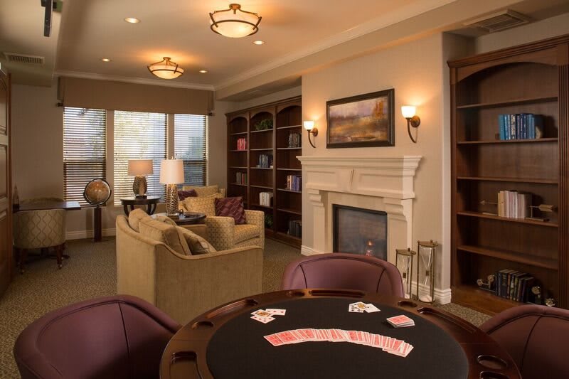 A cozy living room with a poker table and a fireplace, surrounded by comfortable sofas and bookshelves.