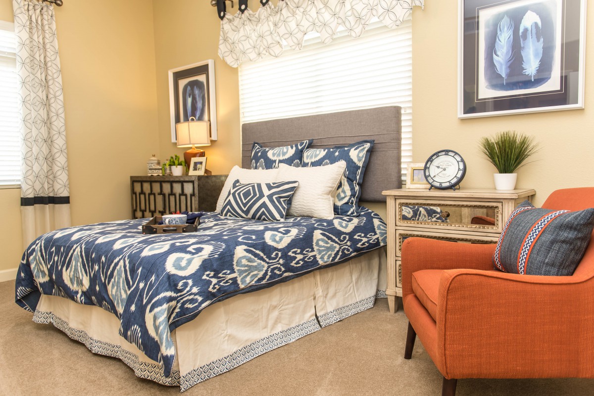 A cozy and well-decorated bedroom featuring a patterned bedspread, an orange armchair, and stylish nightstands with lamps.