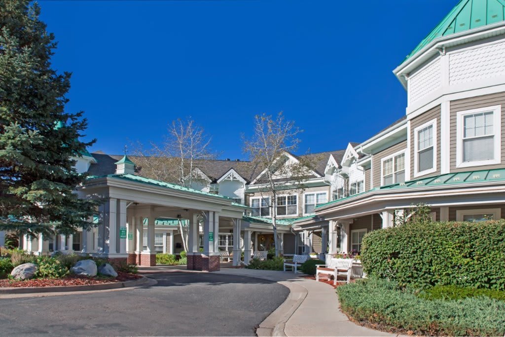 A charming residential building with a wraparound porch and landscaped surroundings.