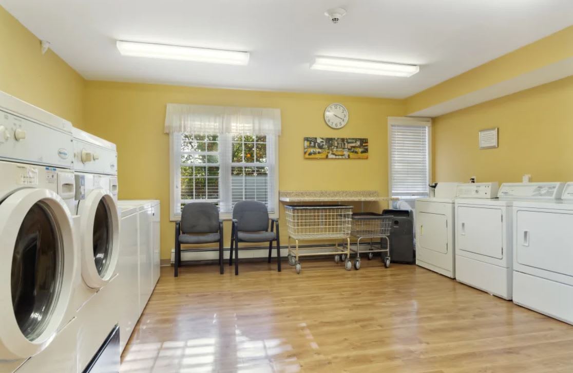 A bright and clean laundry room with washing machines, dryers, and seating.