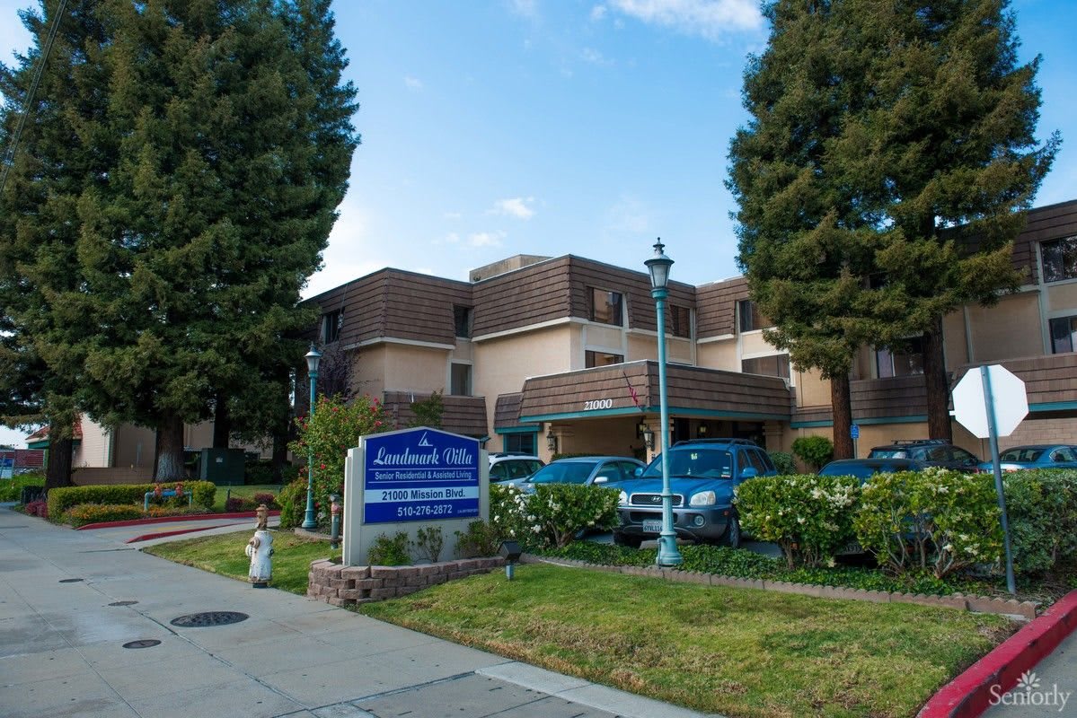 A view of a multi-story building with a sign in front, surrounded by trees and parked cars.