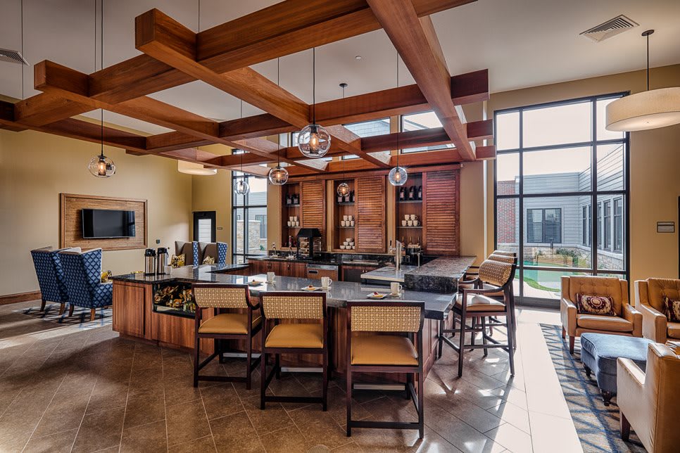 A spacious modern kitchen with wooden beams, an island counter, and bar stools, illuminated by natural light from large windows.
