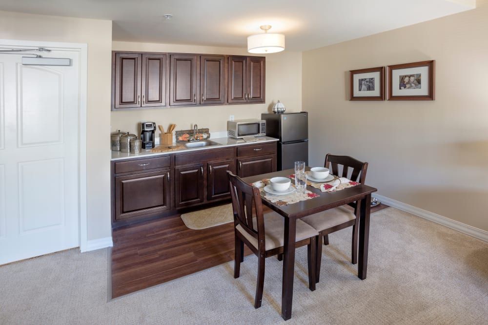 A compact kitchen and dining area with a small table set for two, featuring dark wood cabinets and modern appliances.