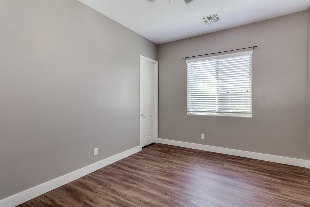 An empty room with wood flooring, a window with blinds, and neutral-colored walls.