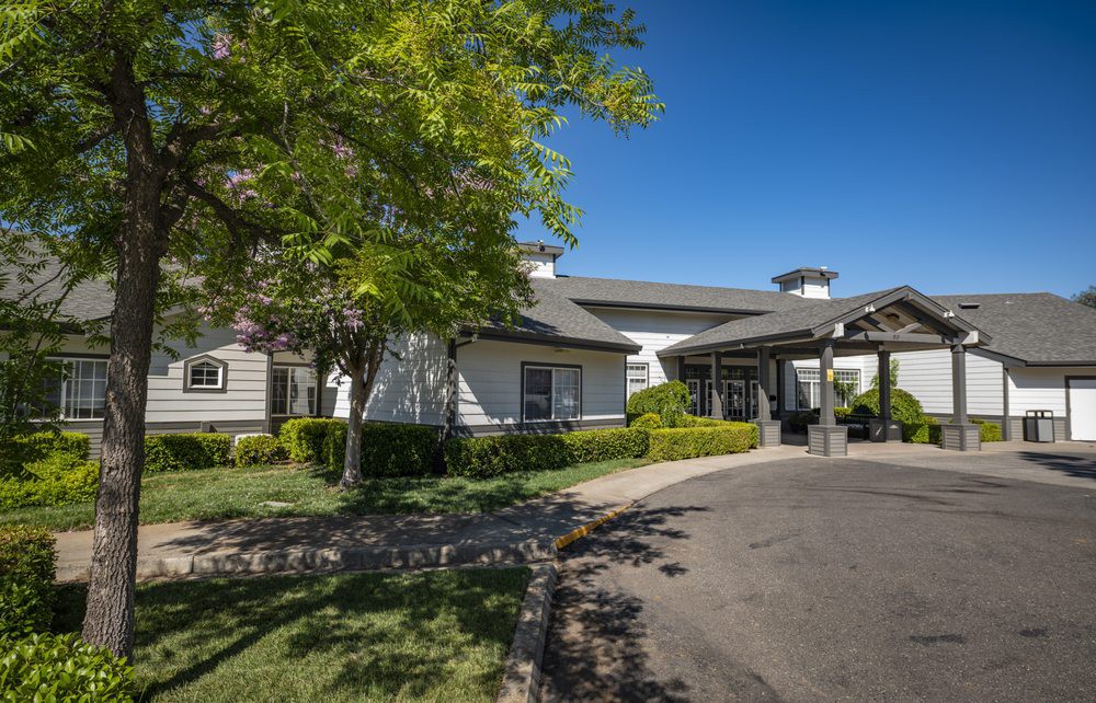A well-maintained house with a driveway, surrounded by trees and landscaping under a clear blue sky.