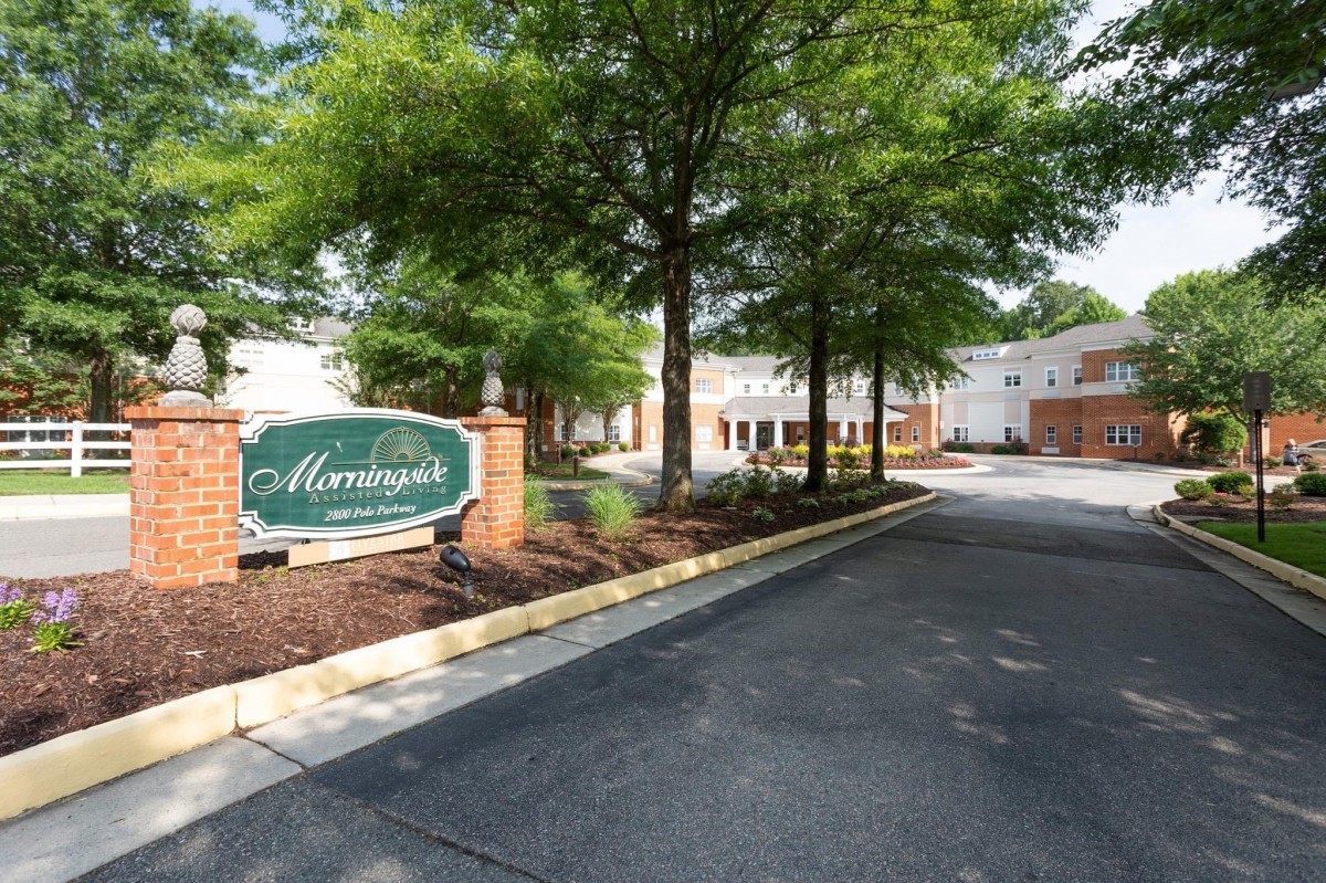 Entrance to a residential or commercial complex with a sign and landscaped driveway.
