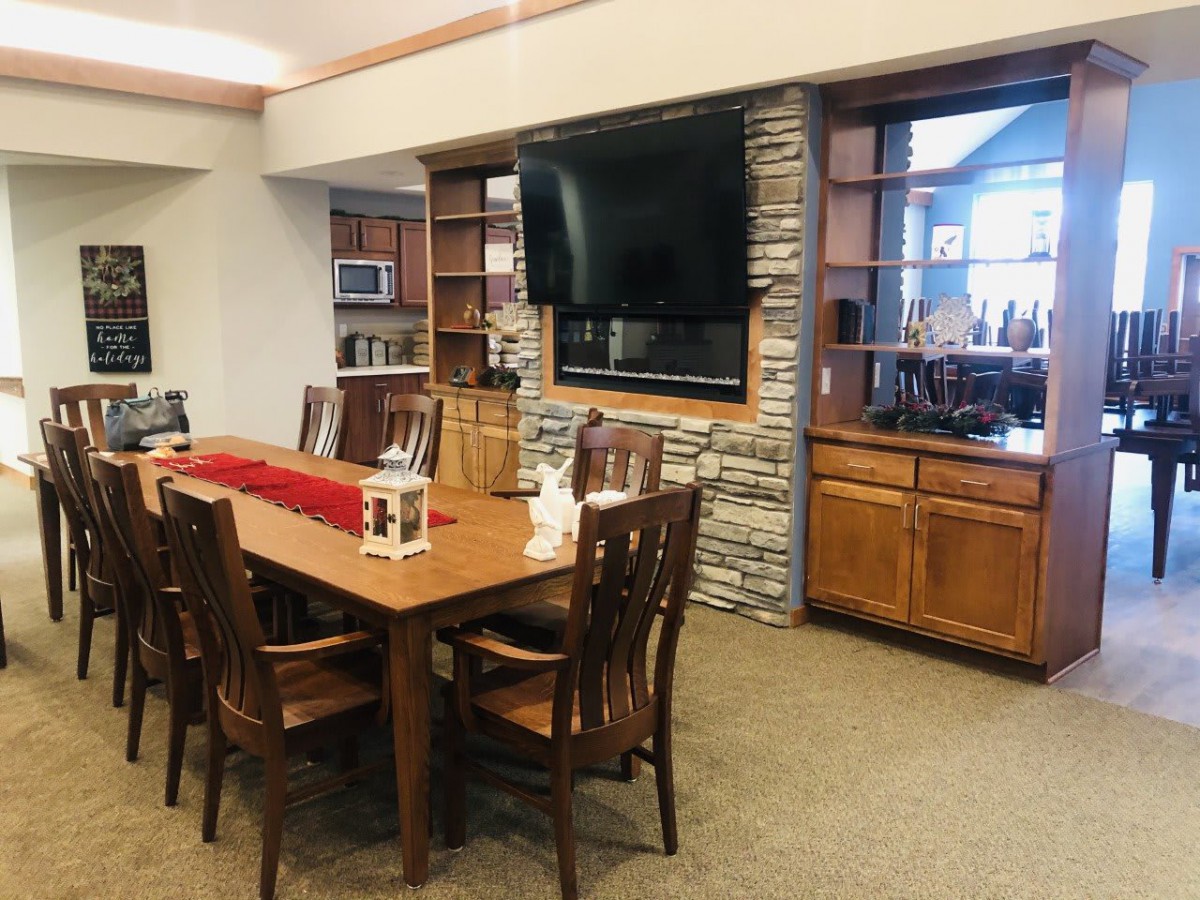 A cozy dining room featuring wooden furniture, a mounted television on a stone-accented wall, and decorative shelving.