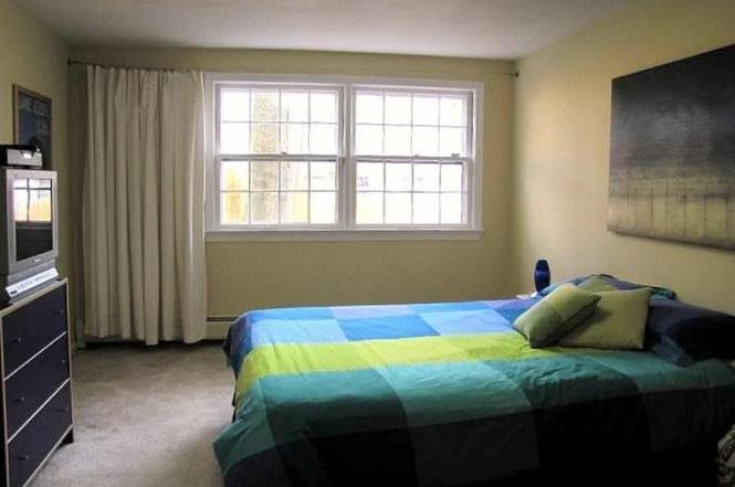 A simple bedroom with a colorful bedspread and large windows letting in natural light.