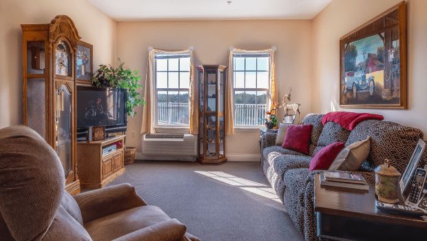 A cozy living room with a sofa, television, and large windows letting in natural light.
