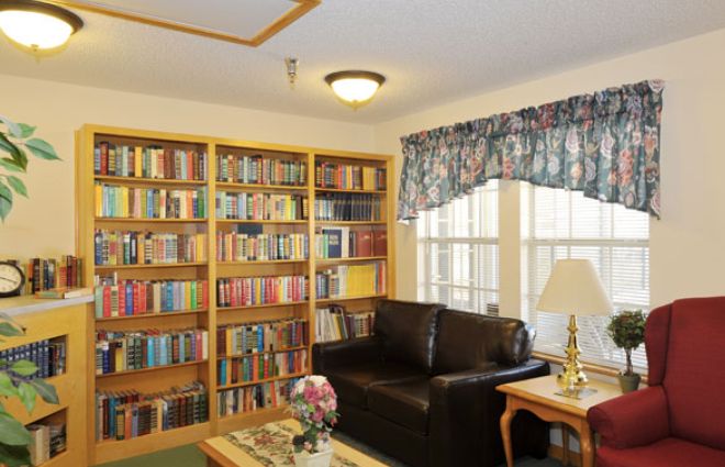 A cozy living room featuring a leather couch, a coffee table with flowers, and a well-stocked bookshelf by the window.
