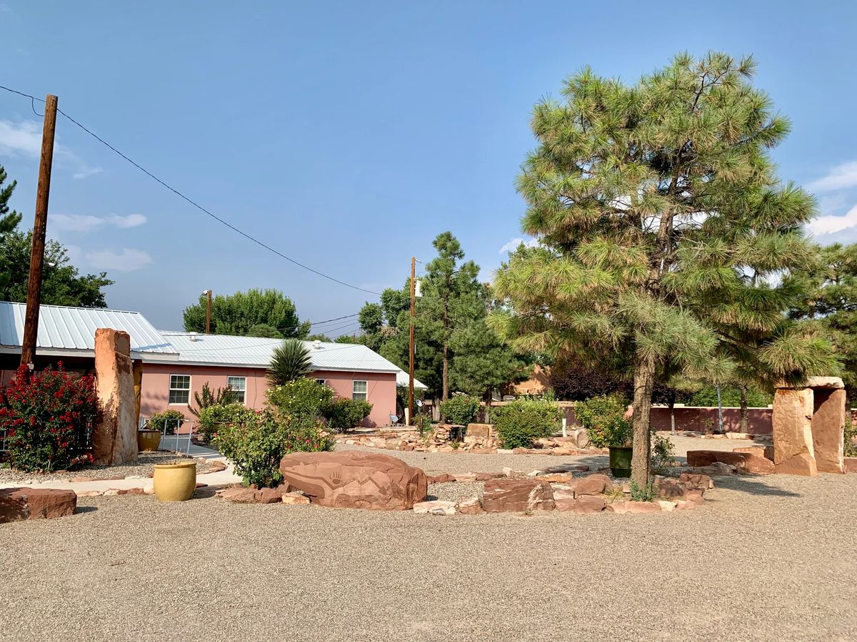 A rustic house surrounded by trees in a desert landscape under a clear blue sky.