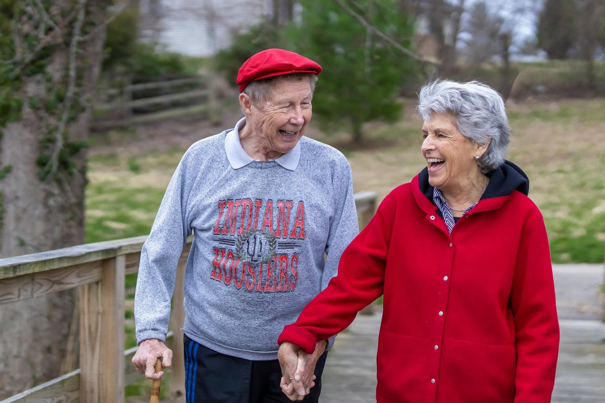 An elderly couple walking hand in hand, smiling and enjoying the outdoors.