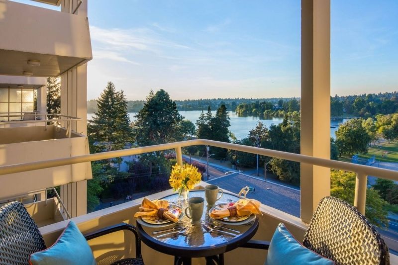 A scenic outdoor breakfast setup on a balcony overlooking a lake and trees on a sunny day.