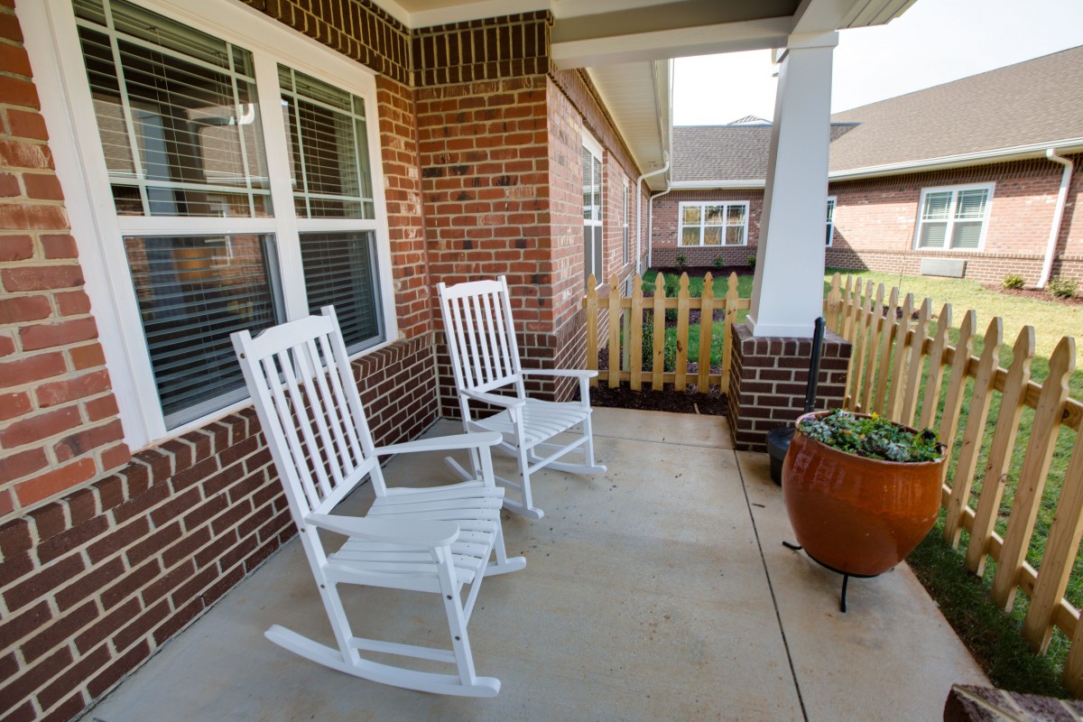A cozy porch featuring two white rocking chairs against a brick wall, perfect for relaxation.