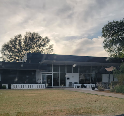 A modern single-story house with large windows, set against a cloudy sky.