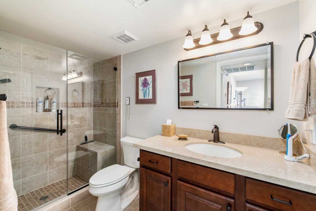 A modern bathroom featuring a glass-enclosed shower, wooden vanity with a sink, a toilet, and a large mirror under elegant light fixtures.