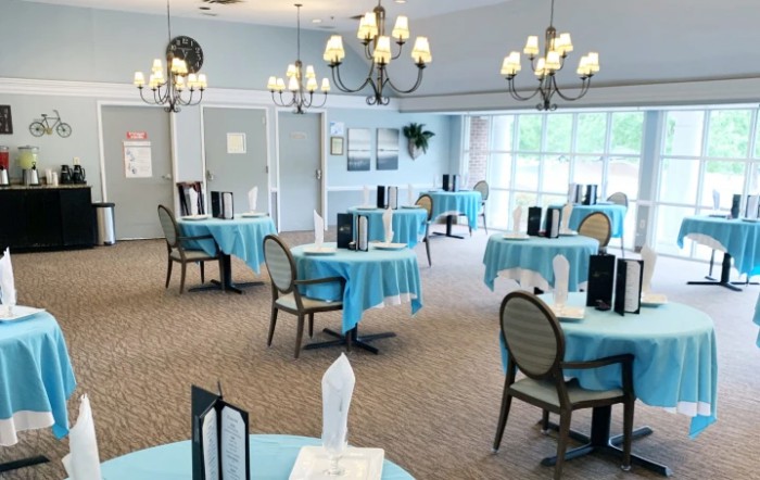 A brightly lit dining area with round tables covered in blue tablecloths and elegant chandeliers hanging from the ceiling.