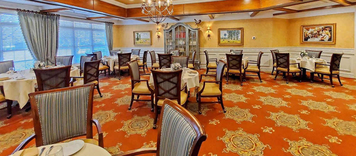 An elegant dining room with neatly arranged tables and chairs, featuring a warm carpet and decorative chandelier.