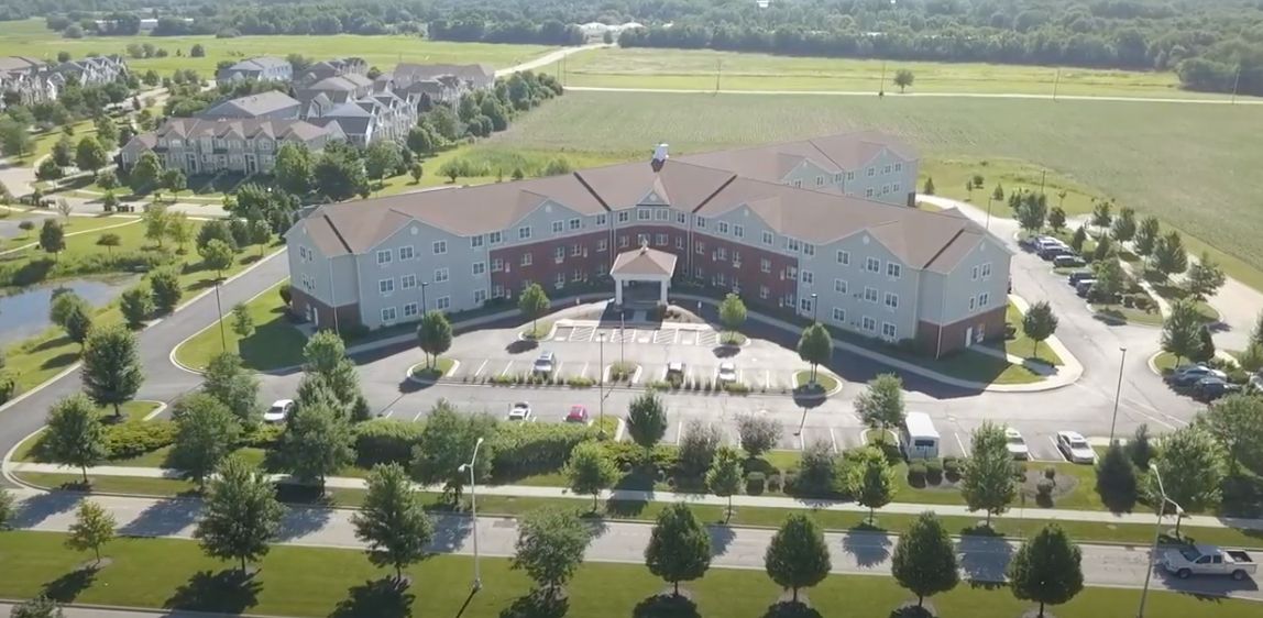 Aerial view of a large residential building with a surrounding landscape of trees and a parking lot.