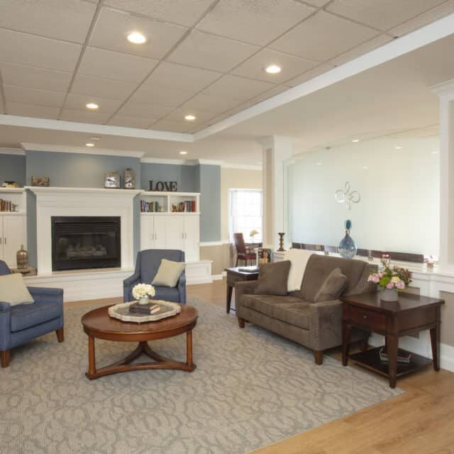 A modern living room featuring a cozy fireplace, with a sofa and armchairs surrounding a wooden coffee table on a patterned carpet.