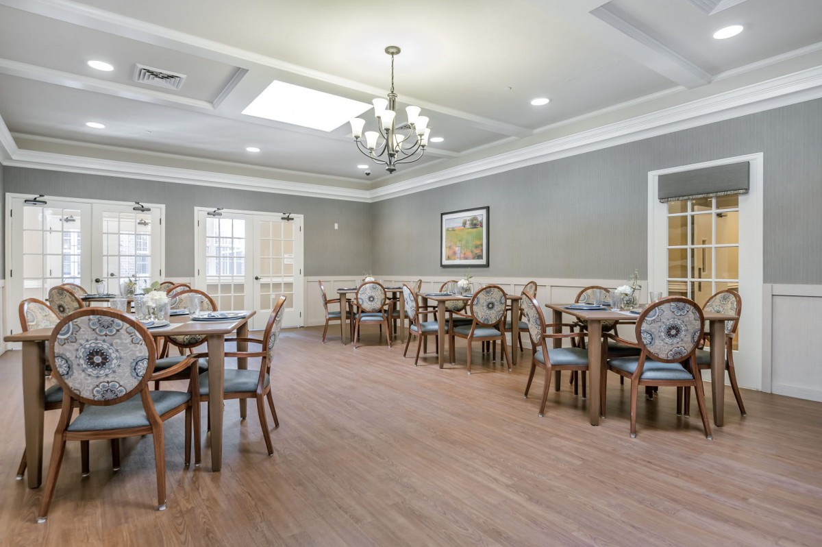 A spacious and elegantly designed dining room with multiple tables and chairs, featuring a chandelier and wooden flooring.