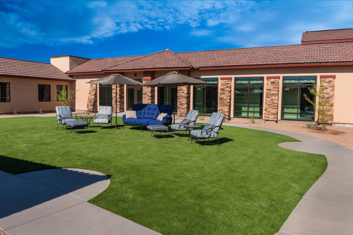 A sunny patio area with seating arrangements and umbrellas on a well-maintained lawn.