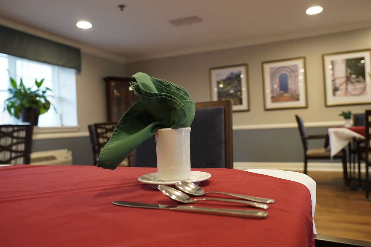A dining table set with a green napkin in a cup and cutlery arranged neatly on a red tablecloth.