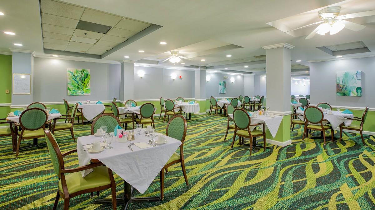 A spacious restaurant interior with neatly arranged tables and chairs, featuring a vibrant carpet design.