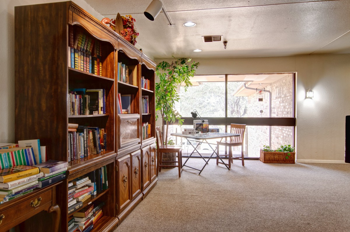 A cozy study room with a wooden bookshelf, desk, and large window view.