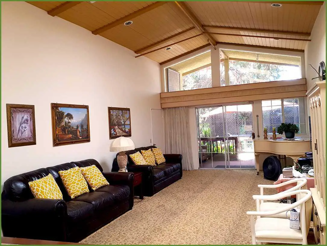 A spacious living room with a high ceiling, featuring comfortable sofas, decorative artwork on the walls, and large windows allowing natural light to fill the space.