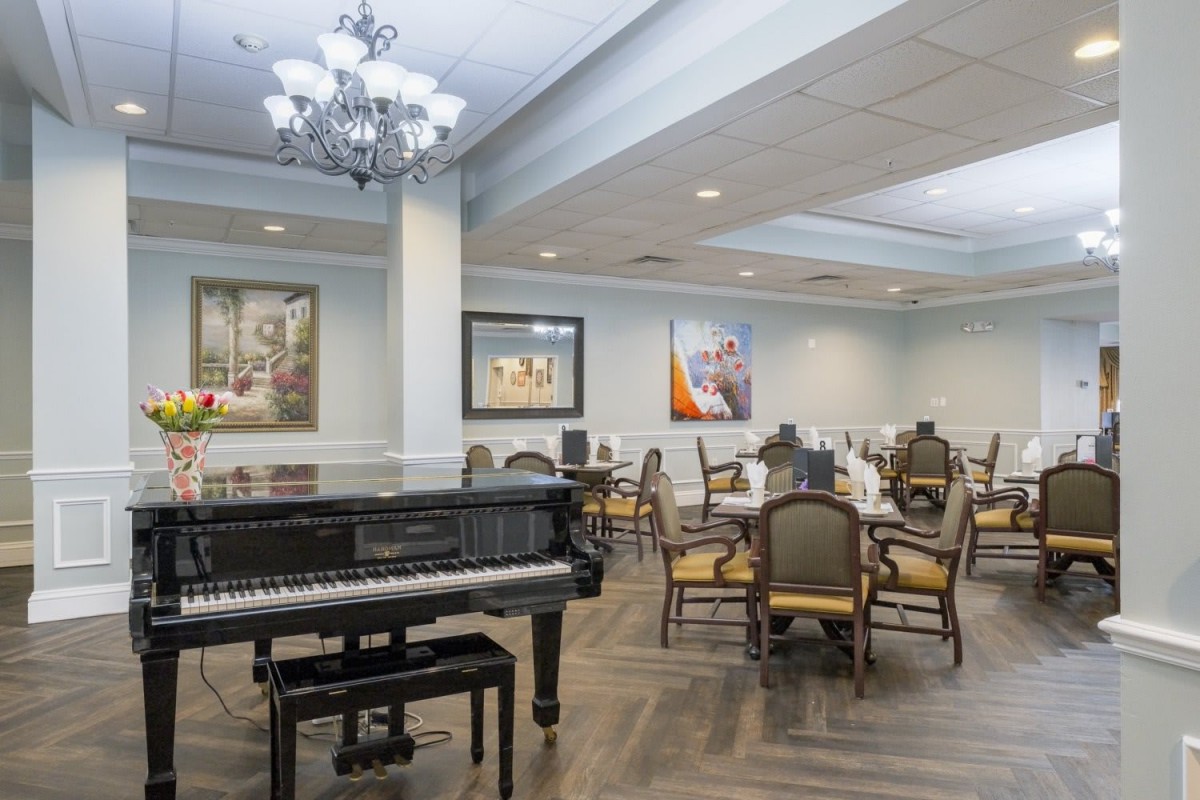 A well-appointed dining room featuring a grand piano, elegant chandeliers, and tastefully arranged tables and chairs with artwork adorning the walls.