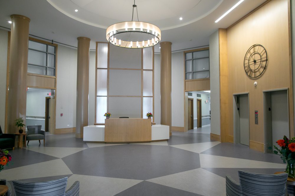 A modern lobby with a central reception desk and a large chandelier.