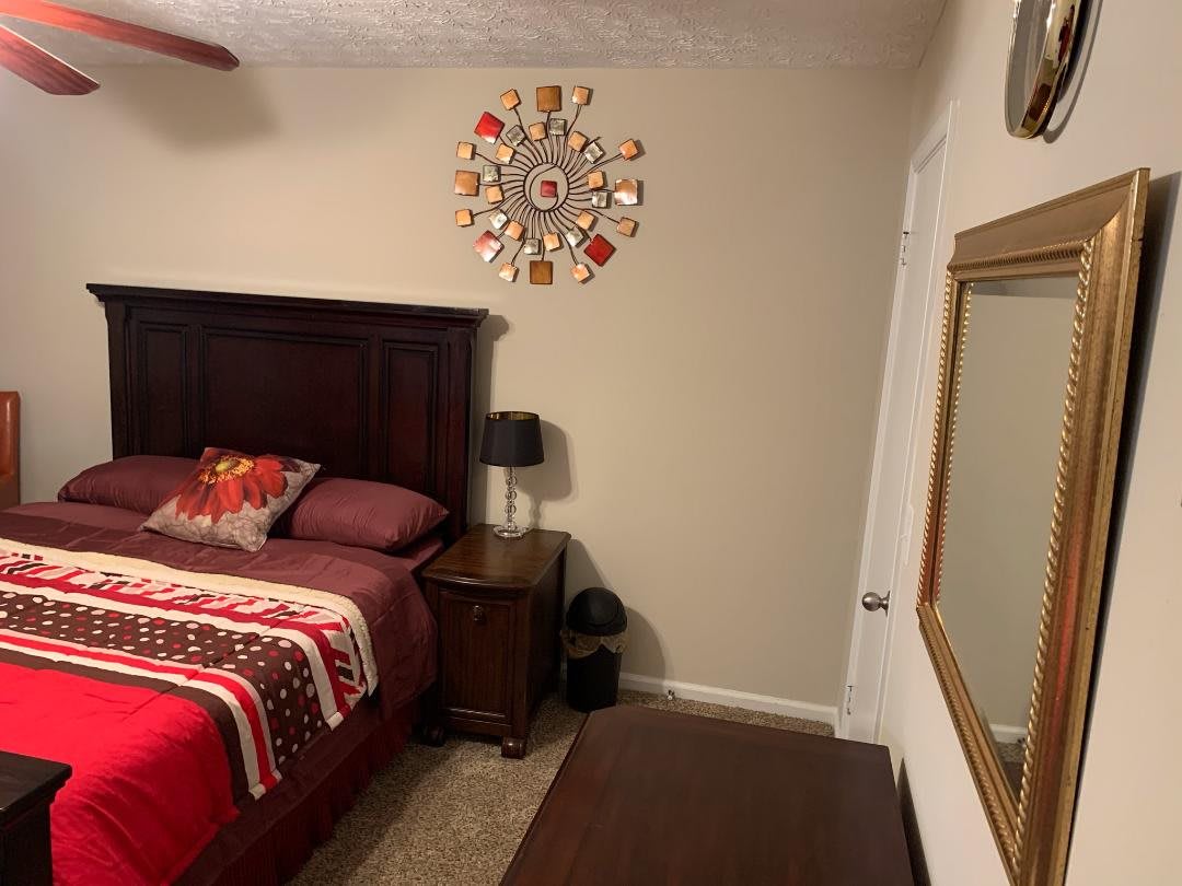 A cozy bedroom with a decorative wall clock, mirror, and wooden furniture.