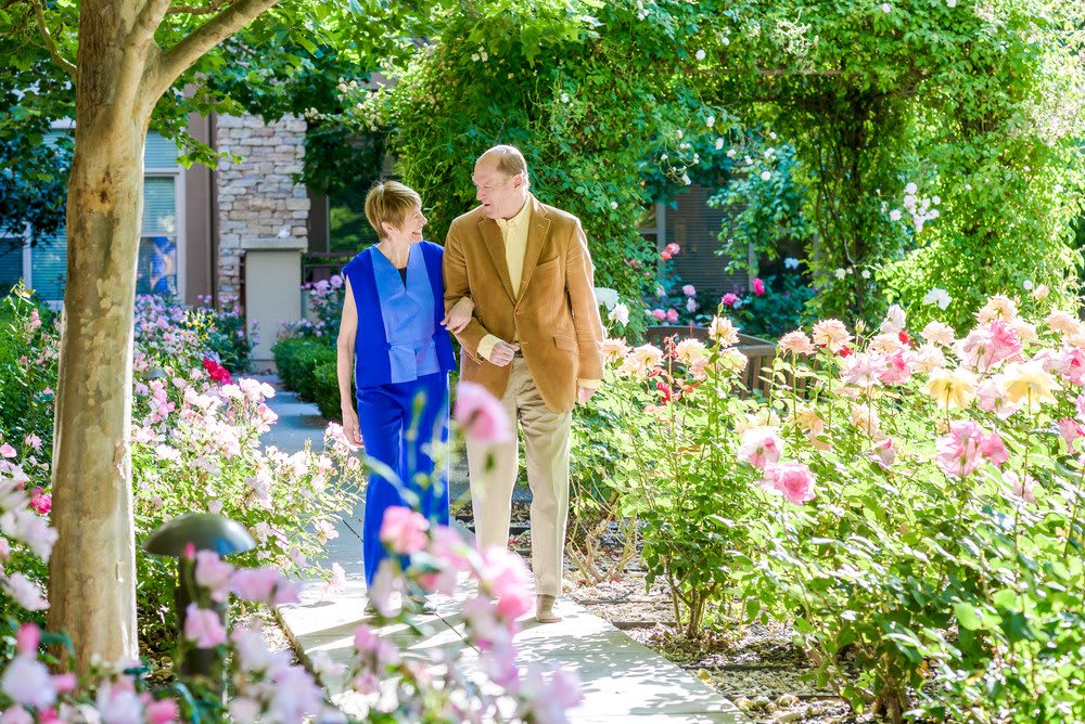 A couple walking together through a beautiful flower garden on a sunny day.