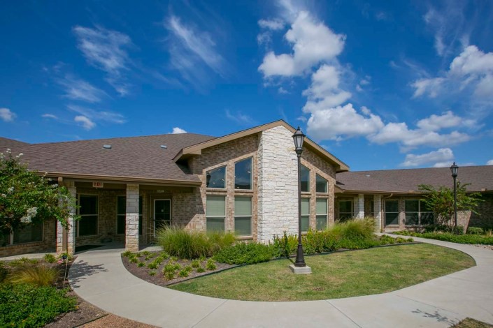 A suburban residential building with a manicured lawn and clear blue skies overhead.