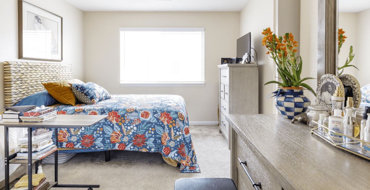 A bright bedroom with a floral bedspread and modern furniture.