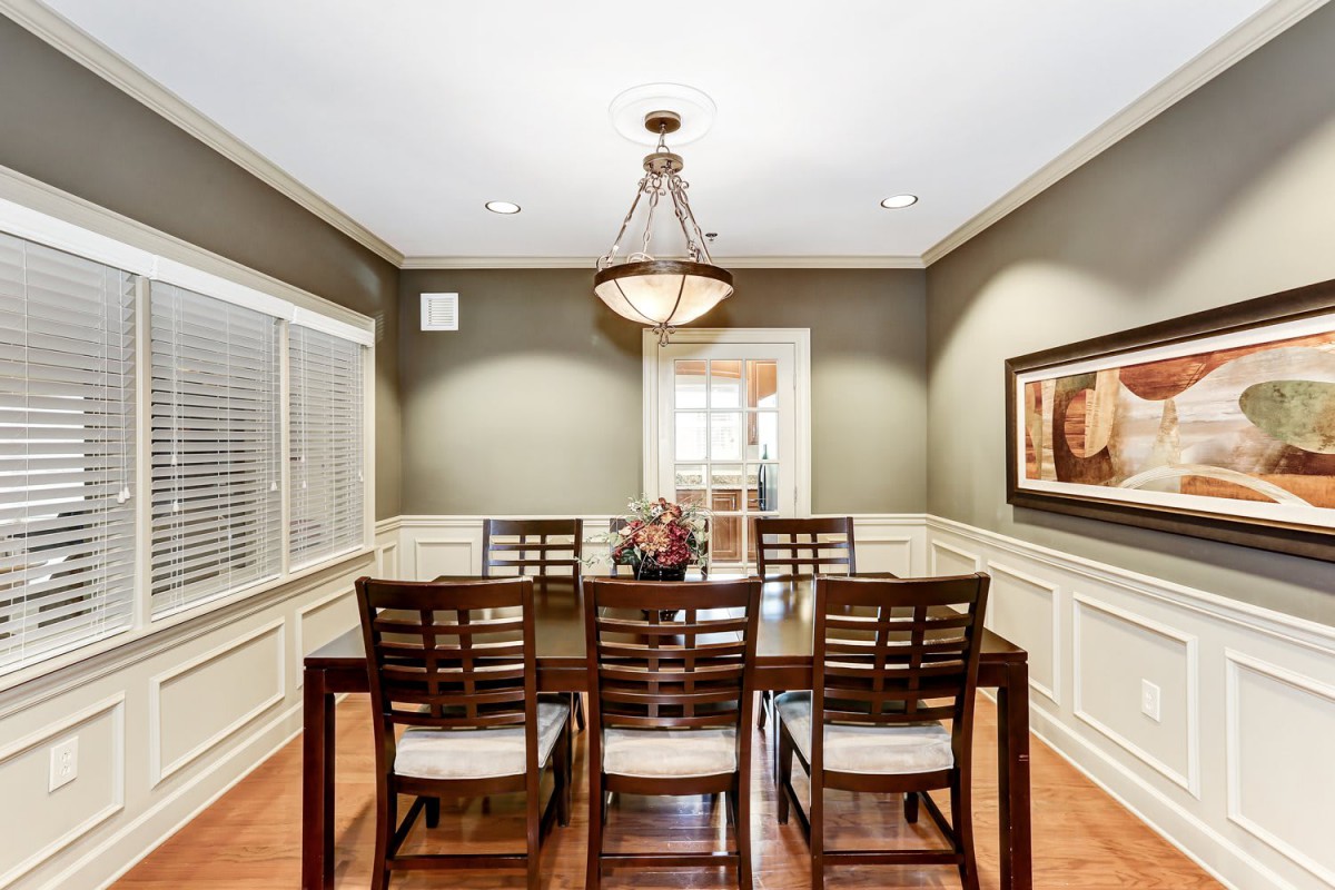 A well-lit dining room with a wooden table and chairs under a traditional chandelier.
