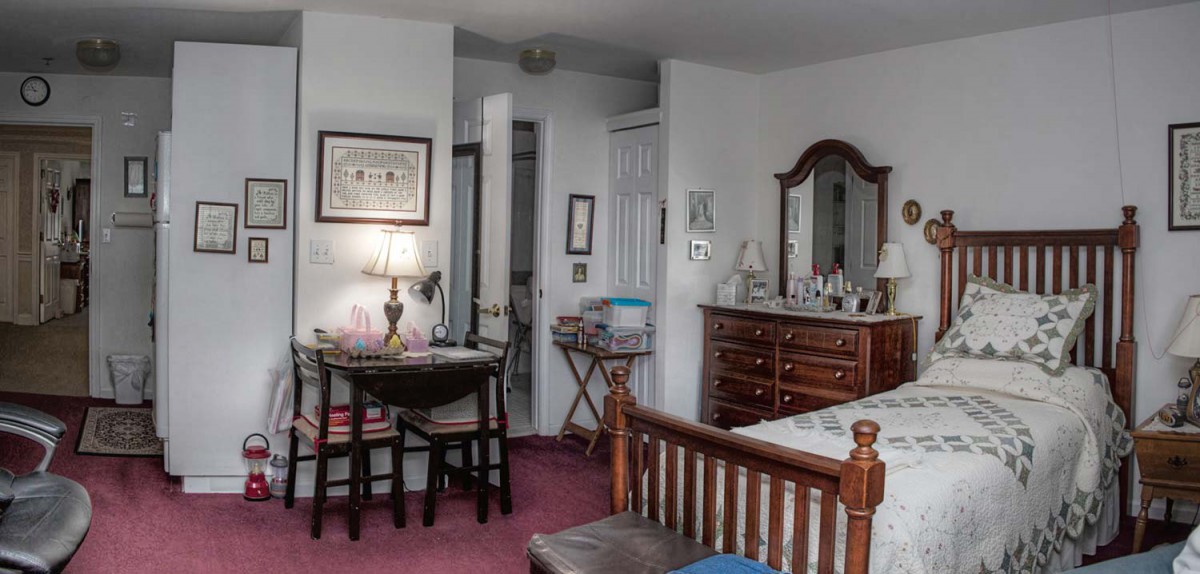 A cozy bedroom with a dresser, mirror, lamp, and small table with chairs.